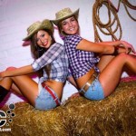 two women sitting back to back on a bale of hay